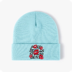 Detail of red lips embroidery and text on light blue knitted beanie hat