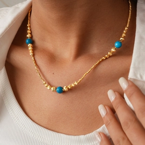 Detail of 18K gold beaded necklace with blue stones on a model's neck for elegant styling