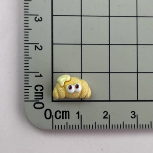 Mini resin croissant charm with cartoon eyes shown on a scale for size measurement