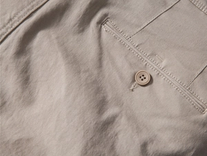 Detail of khaki cotton trousers featuring reinforced pocket stitching and a matching button