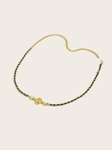 Detail of gold metal and black leather woven chain belt with round badge and pearls