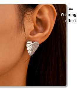 Close-up of heart leaf textured stud earrings in silver finish on model ear
