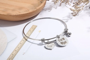 Detailweergave van de zilveren verstelbare roestvrijstalen armband met hart en bedeltjes