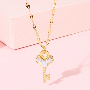 Detailed close-up of golden key pendant with white shell inlay on a soft pink surface