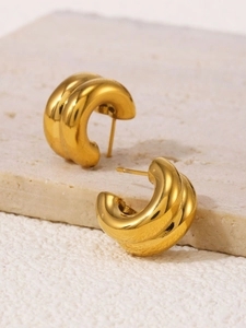 Detail view of double-layered gold C-shape stud earrings on a textured stone surface