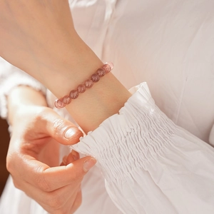 Close-up of a pink strawberry quartz beaded bracelet worn by a model on a white background
