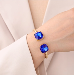 Detail of a gold cuff bracelet featuring two square-cut blue stones worn on a model's wrist
