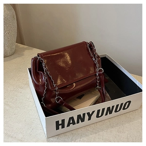 Détail d'un sac bandoulière en cuir verni rouge foncé avec chaîne argentée en boîte
