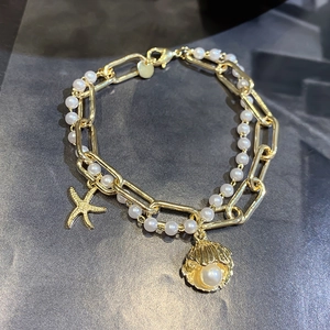 Detail of gold starfish and shell charms on double-layer pearl and chain bracelet
