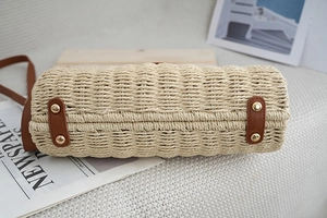 Detailed base view of woven straw beach bag featuring brown leather strips and metal rivets