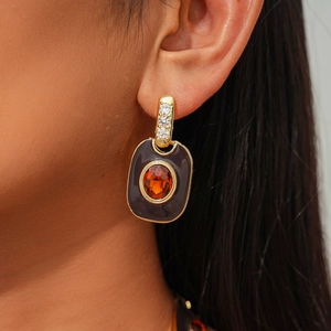Detail of vintage gold ear studs with dark gray enamel and orange gemstone