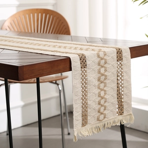 Boho woven table runner with hollow geometric patterns and fringe on a wooden table