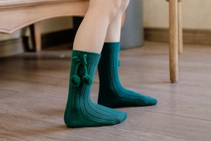 Detail of forest green knee-high baby socks with ribbed texture and side pom-poms