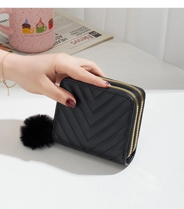 Detail view of women's black quilted double zipper wallet with decorative fur pompom