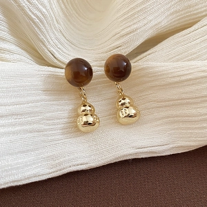 Detail of vintage gold gourd earrings with round tiger eye stones on brown fabric