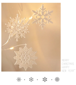 Close-up of three glittery white snowflake ornaments hanging on a warm lit tree