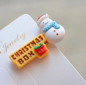 Detail of Christmas snowman hair clip with yellow Christmas Box ornament on card