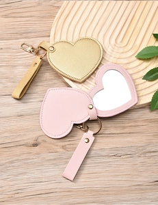 Detail of heart-shaped leather portable mirrors in gold and pink on a wooden tray