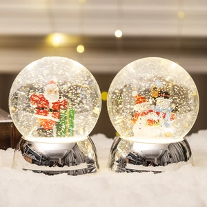 Illuminated Christmas snow globe with Santa and silver base on warm bokeh background