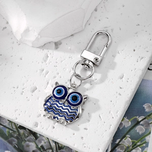 Macro shot of owl alloy keychain with blue evil eye details on a white textured stone