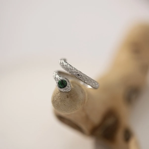 Silver snake ring with scale texture and green malachite eye on a rustic wood piece