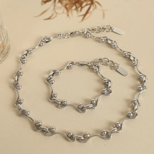 Titanium steel jewelry set with wavy links, round beads and Lucky tag on beige background