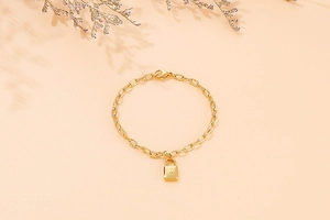Detailed close-up of a gold padlock pendant bracelet with engraved starburst pattern