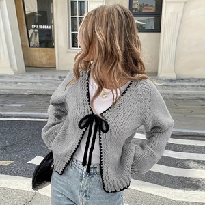 Detailed knit texture of a grey cardigan featuring black crochet trim and bow tie closure