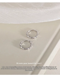 Detailed view of silver bamboo-style hoop earrings on elegant beige texture with soft veil