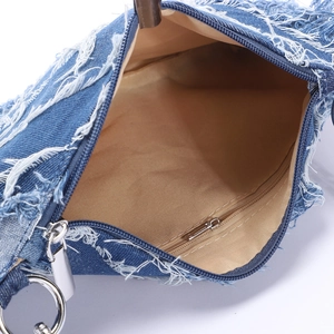 Detail view of denim fringe bag showing beige lining, silver zipper, and interior pocket