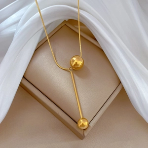 Close-up of gold Y-shaped tassel necklace with metal beads on beige silk background
