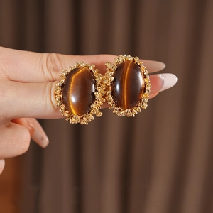 Close-up of vintage tiger eye earrings with golden textured metal rim on brown fabric