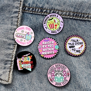 Collection of horror movie lover enamel pins displayed on a blue denim jacket surface