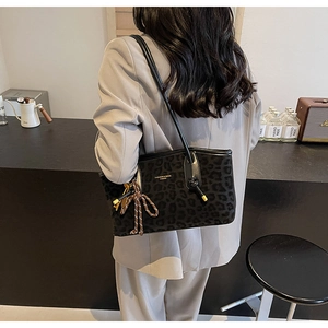 Détail d'un sac cabas léopard avec pompon et logo doré dans un décor de café moderne