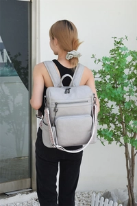 Detail of grey leather backpack featuring woven patterned straps and decorative tassels