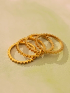 Detail view of four stacked gold stainless steel gear rings with polished finish