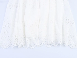 Detailed close-up of intricate white broderie anglaise embroidery on a scalloped hemline