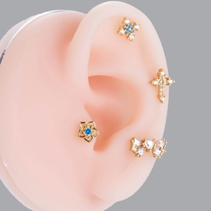 Detailed view of gold screw-back studs with butterfly, cross and blue zircon butterfly motifs