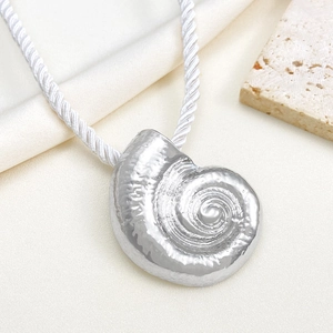 Detail of silver conch shell pendant on white braided cord over beige stone