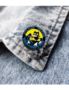 Close-up of cat enamel pin on denim jacket collar featuring It's Fine text design
