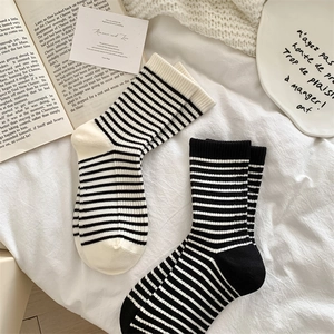 Detail of black and white striped wool blend crew socks on a soft white bedsheet