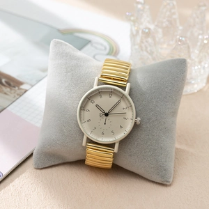 Gros plan d'une montre vintage avec cadran crème et bracelet extensible doré sur coussin
