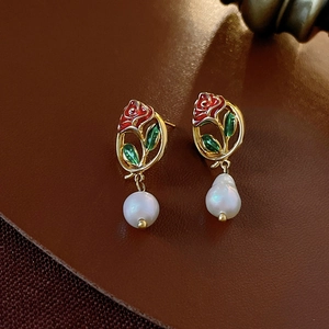 Macro shot of vintage gold earrings with red enamel rose and white baroque pearls