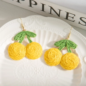 Handmade woven cherry drop earrings with yellow fiber fruit and green leaves on white plate