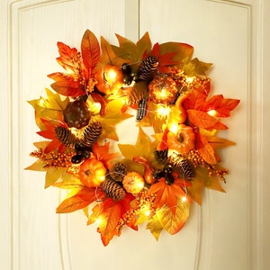 Artificial maple leaf wreath with pumpkins, pine cones, and warm LED lights on a white door