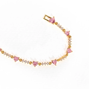 Macro detail of gold-plated bracelet with pink heart-shaped stones and zircons