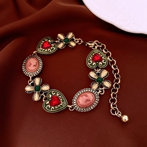 Macro shot of vintage gold bracelet with red heart gem and pink cameo on brown silk