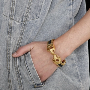 Detail of men's leather bracelet with dual gold skull charms and braided black rope cord