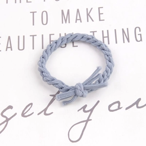 Detail of a braided misty blue elastic hair tie with a knot, shown on a clean paper background