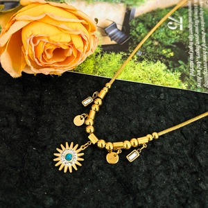 Gold stainless steel sun pendant necklace with blue gemstone on black textured background